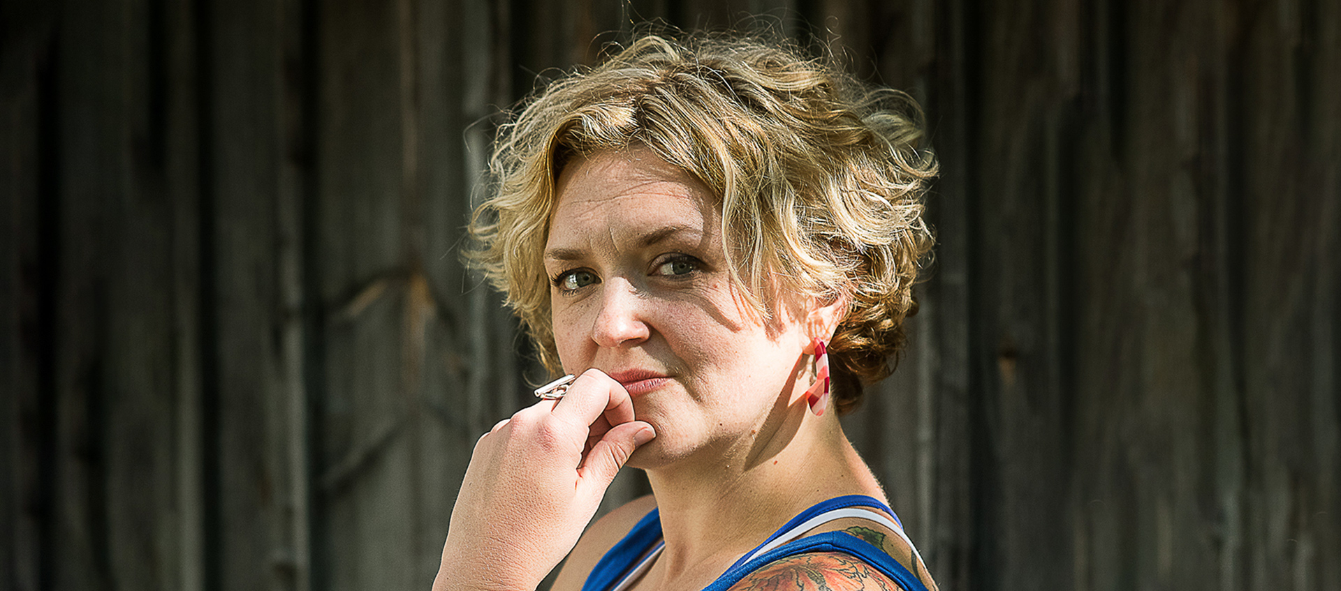 A photo of Abby Zbikowski in front of a darker background. Abby's left hand touches their chin. Abby has short blond/brown hair.