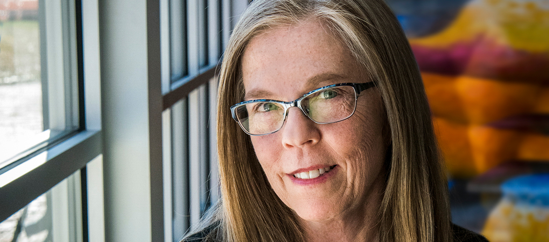 An image of Kari Gunter-Seymour from the neck up. Kari is wearing glasses and sits in front of a window.