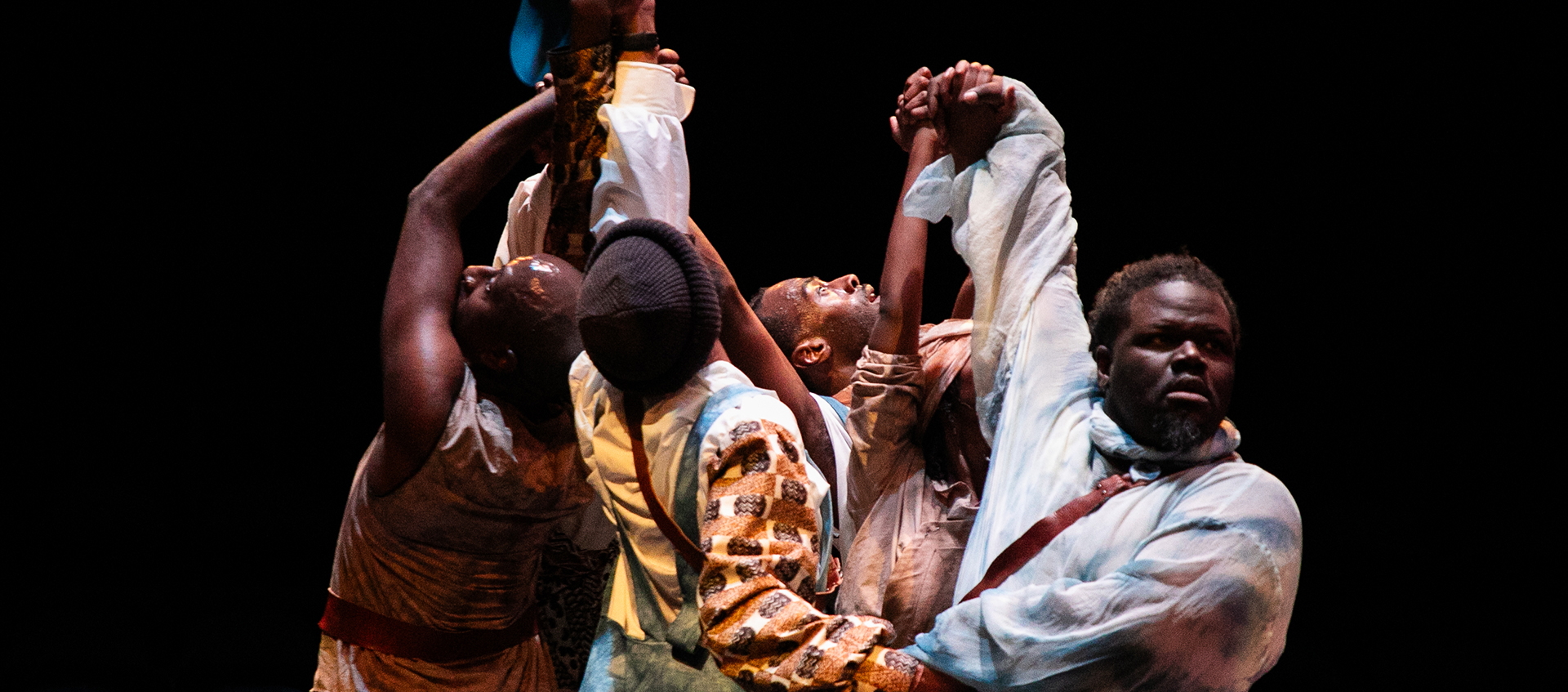 Five Black men stand in a circle, their hands clasped together and held above their heads. 