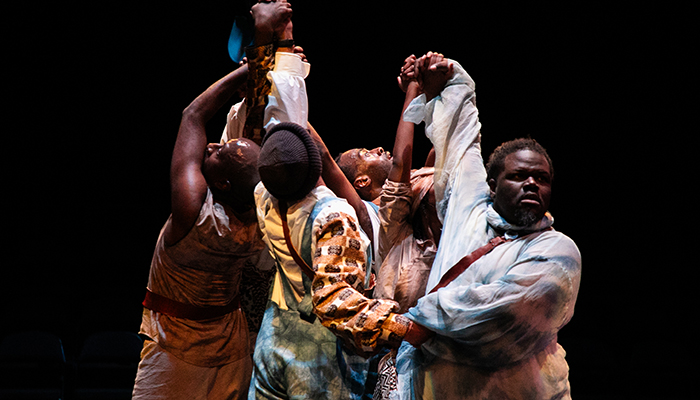 Five Black men stand in a circle, their hands clasped together and held above their heads. 