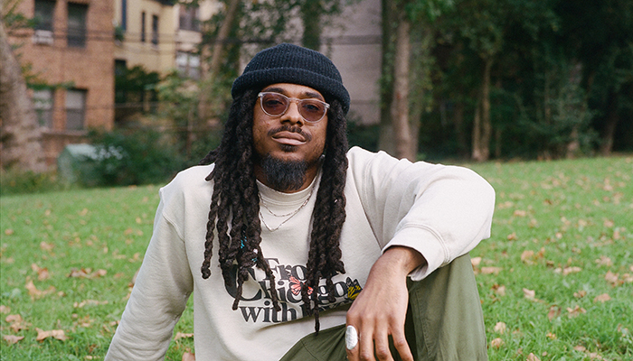 Headshot of Joel Ross. He is sitting on a lawn wearing sunglasses and a beanie.