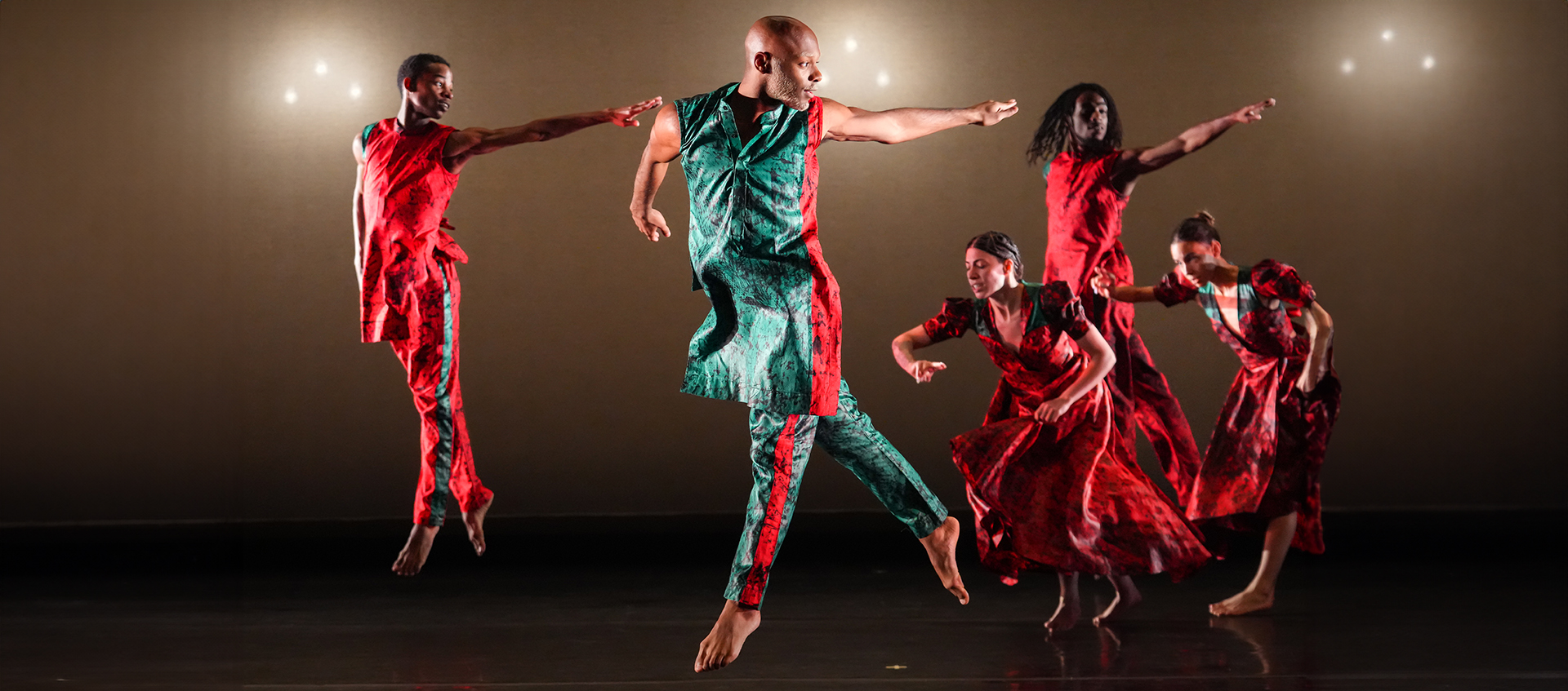 A group of dancers wearing red and blue costumes point to the right.