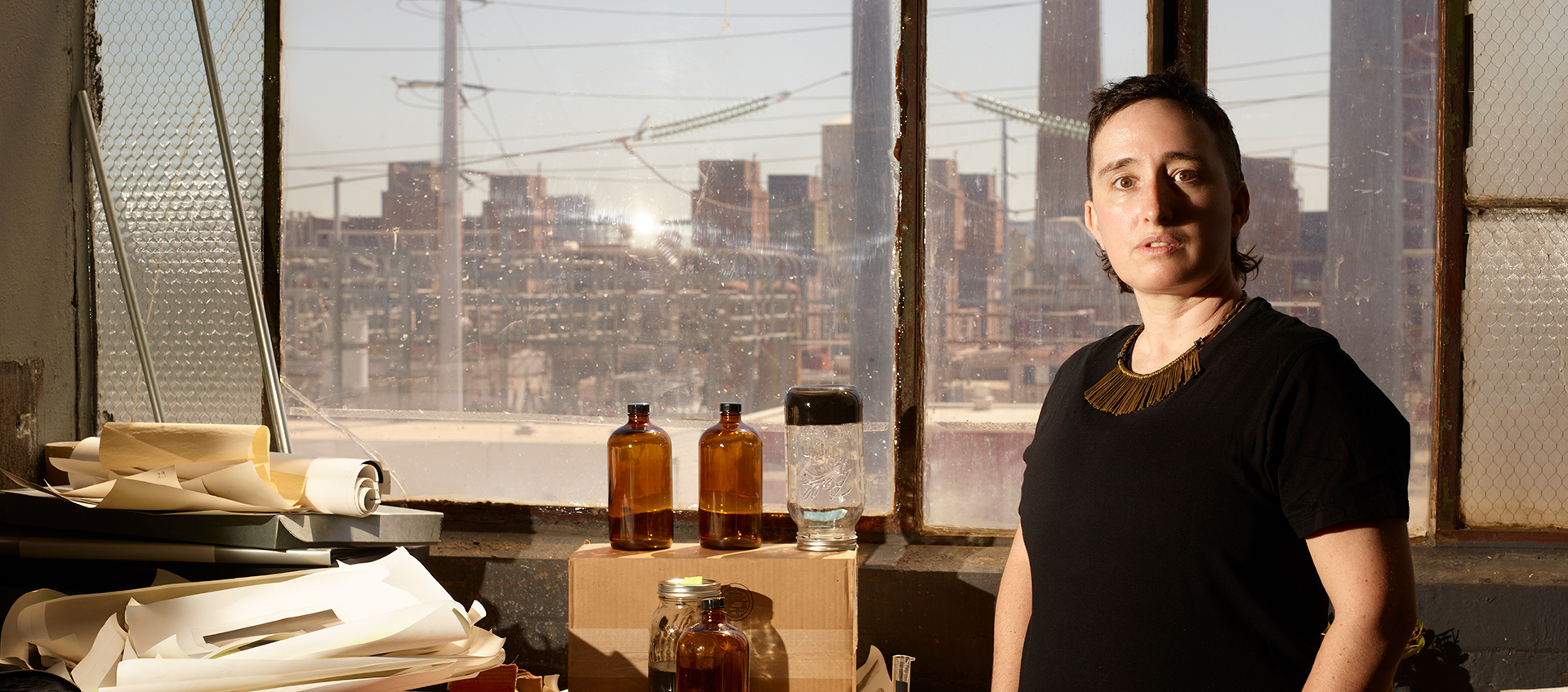 Jonas N.T. Becker stands in an industrial studio with large windows behind them. Jonas has a light skin tone, short dark hair, and wears a dark shirt.