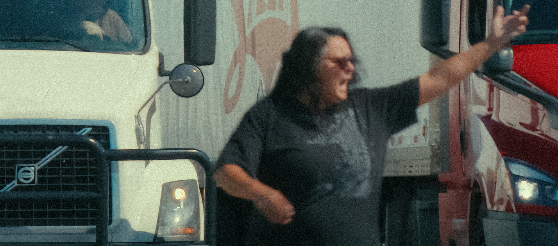 A qoman stands next to a semi truck with her hand in the air. She appears to be yelling.