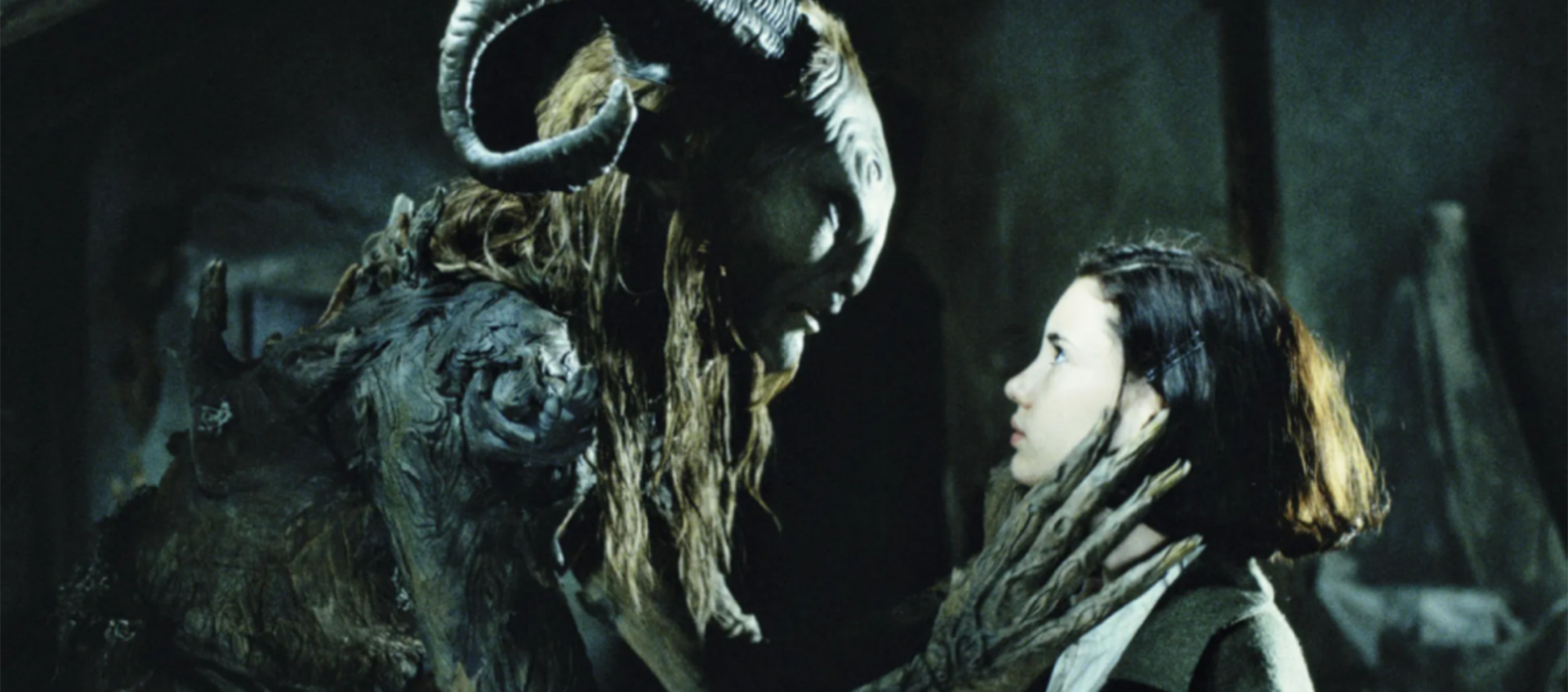 A monster with ram horns and long hair holds a hand with long fingers up to a young girl with brown hair.