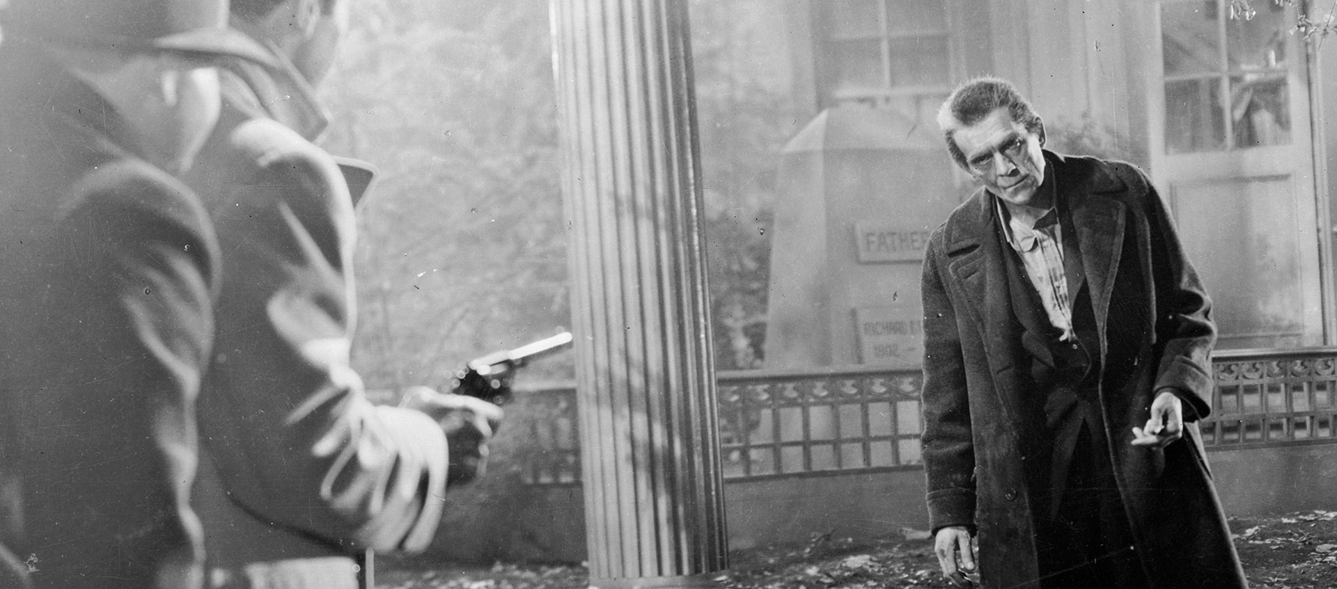 Two men stand in a cemetery pointing a gun at an approaching man.