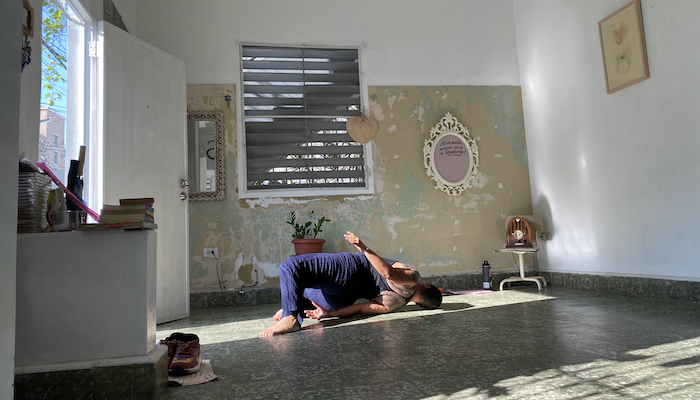 Movement artist Awilda Rodriguez Lora lies on the floor of her home La Rosario in Puerto Rico, her knees bent and her back arched with her left hip lifted off the floor so she's facing away from the camera